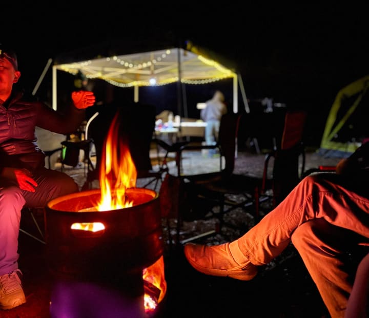 A group sitting around a campfire at night, faces lit by the flames